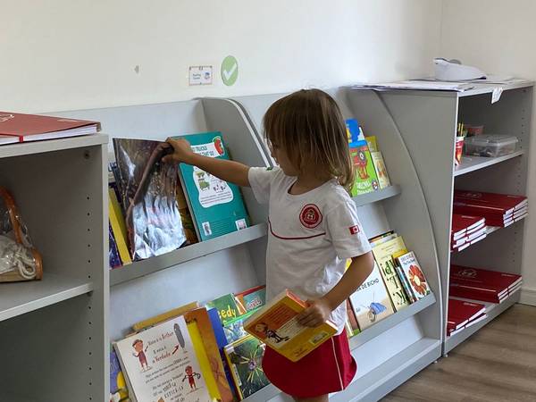 Aluna escolhe um livro na estante da biblioteca bilíngue