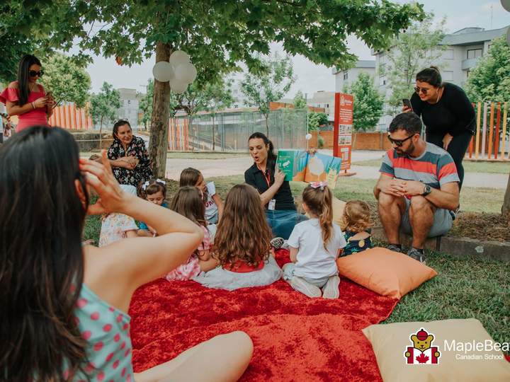 Crianças e professoras em roda de contação de história na grama do pátio da Maple Bear Caxias do Sul