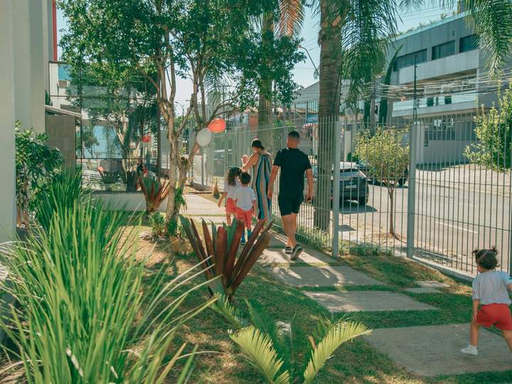 Entrada ajardinada da Maple Bear Caxias do Sul, com famílias chegando à escola
