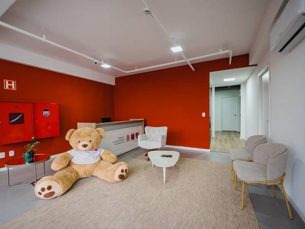 Recepção da escola com parede vermelha e urso de pelúcia da Maple Bear